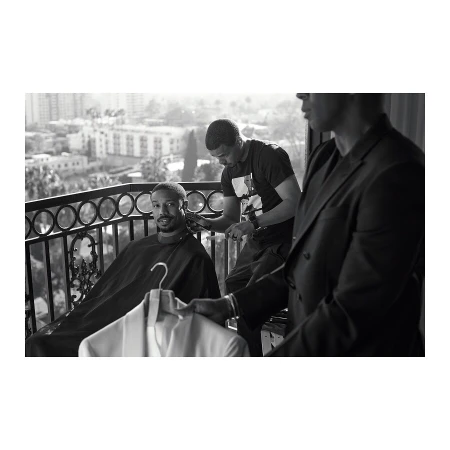 Michael B. Jordan gets a haircut on a balcony overlooking the city, assisted by a barber and a man holding a jacket.