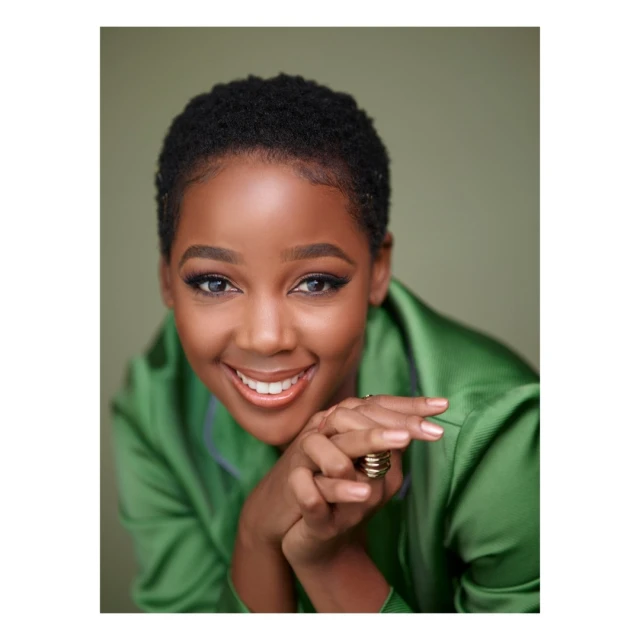 Close-up portrait of an African-American adult woman with short hair, smiling and wearing a green silk top against a green background.