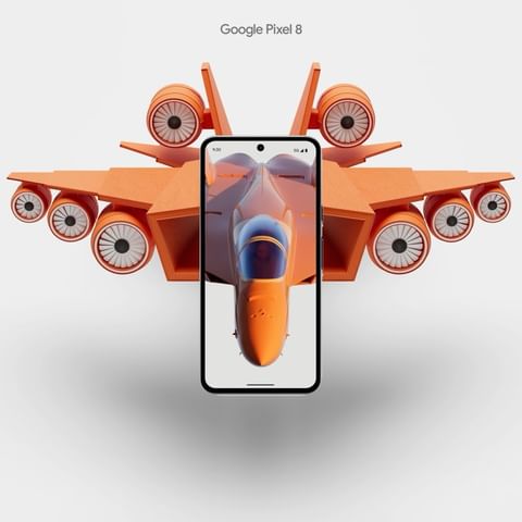 Orange toy fighter jet behind a black smartphone with a display showing an orange fighter jet cockpit against a white background.