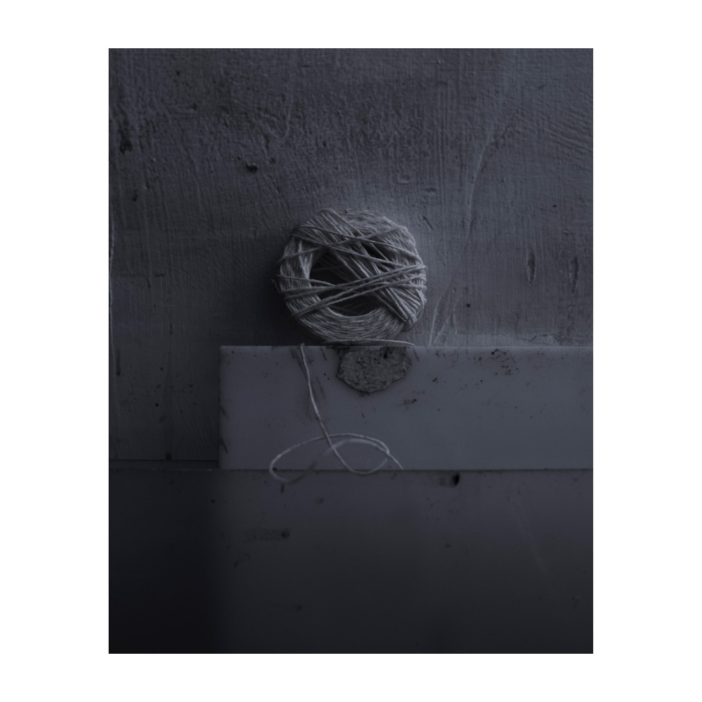 Close-up studio shot features a ball of natural twine resting atop a rectangular platform, set against a textured gray wall backdrop.