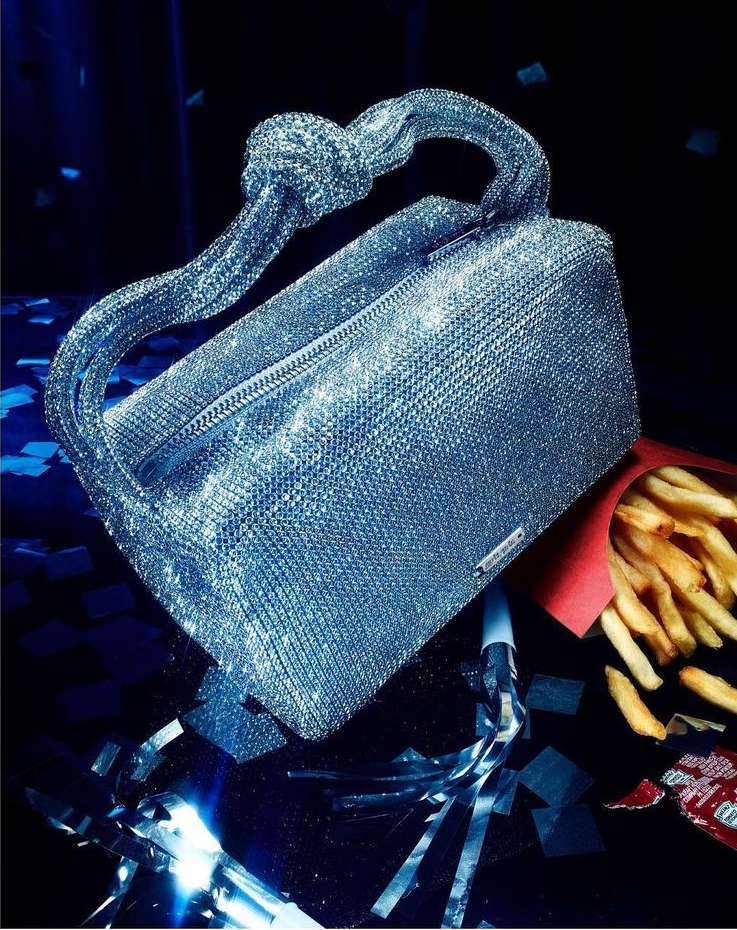 Sparkly silver handbag with knot handle, set with French fries and silver streamers on a dark background. Fashionable accessorization.