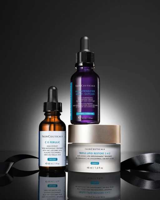 Three SkinCeuticals skincare product bottles and jar are displayed on a reflective surface with a gray ribbon and dark background.