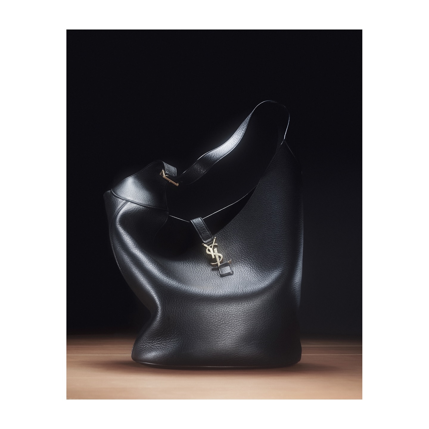 Elegant Saint Laurent hobo bag in black leather with a gold logo, showcased against a dark backdrop with soft, directional lighting.