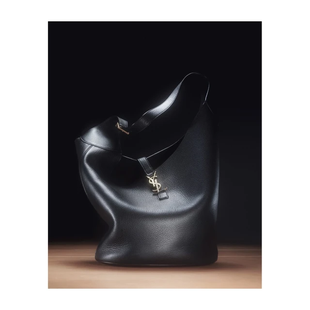 Elegant Saint Laurent hobo bag in black leather with a gold logo, showcased against a dark backdrop with soft, directional lighting.