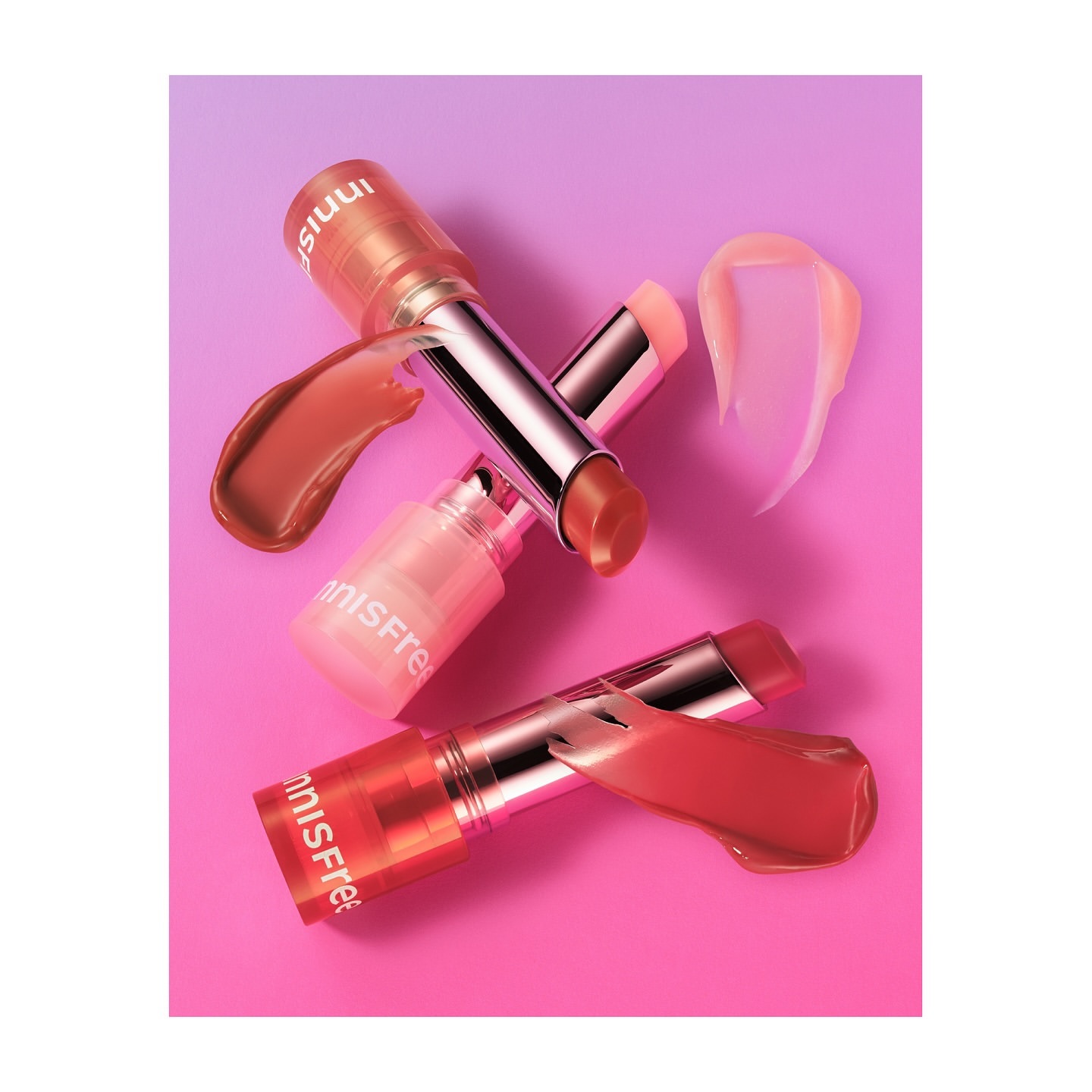 Three Innisfree lip balms are displayed against a bright gradient background of pink and lavender. Cosmetic smears of balm highlight the product.