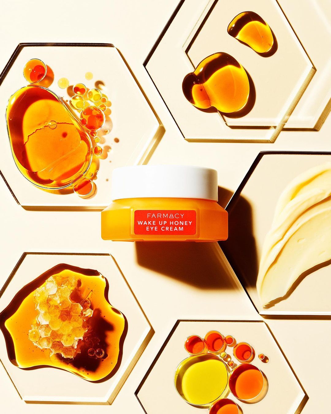 Close-up of Farmacy Wake Up Honey Eye Cream on a beige hexagon tile surrounded by honey and cream, cosmetic flat lay.