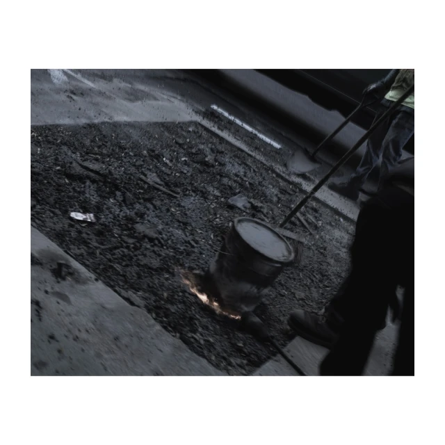 Construction worker performing road repair with molten material and a bucket in an urban environment, grayscale color palette.