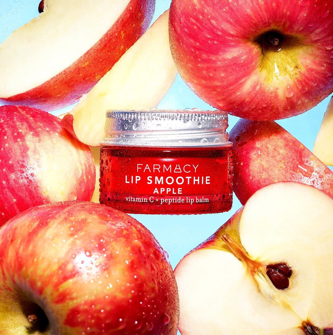 Farmacy Lip Smoothie Apple lip balm jar surrounded by fresh, sliced apples, showcasing a close-up of the product and its natural ingredients.