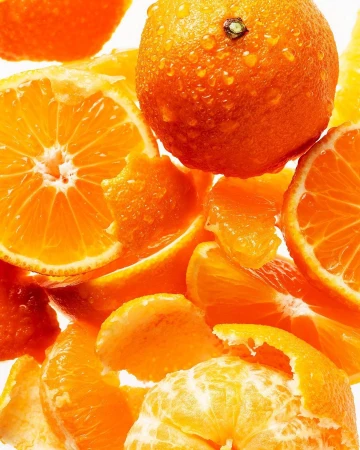 Close-up of fresh tangerines and tangerine slices with water droplets against a bright, white background, showcasing vibrant orange hues.