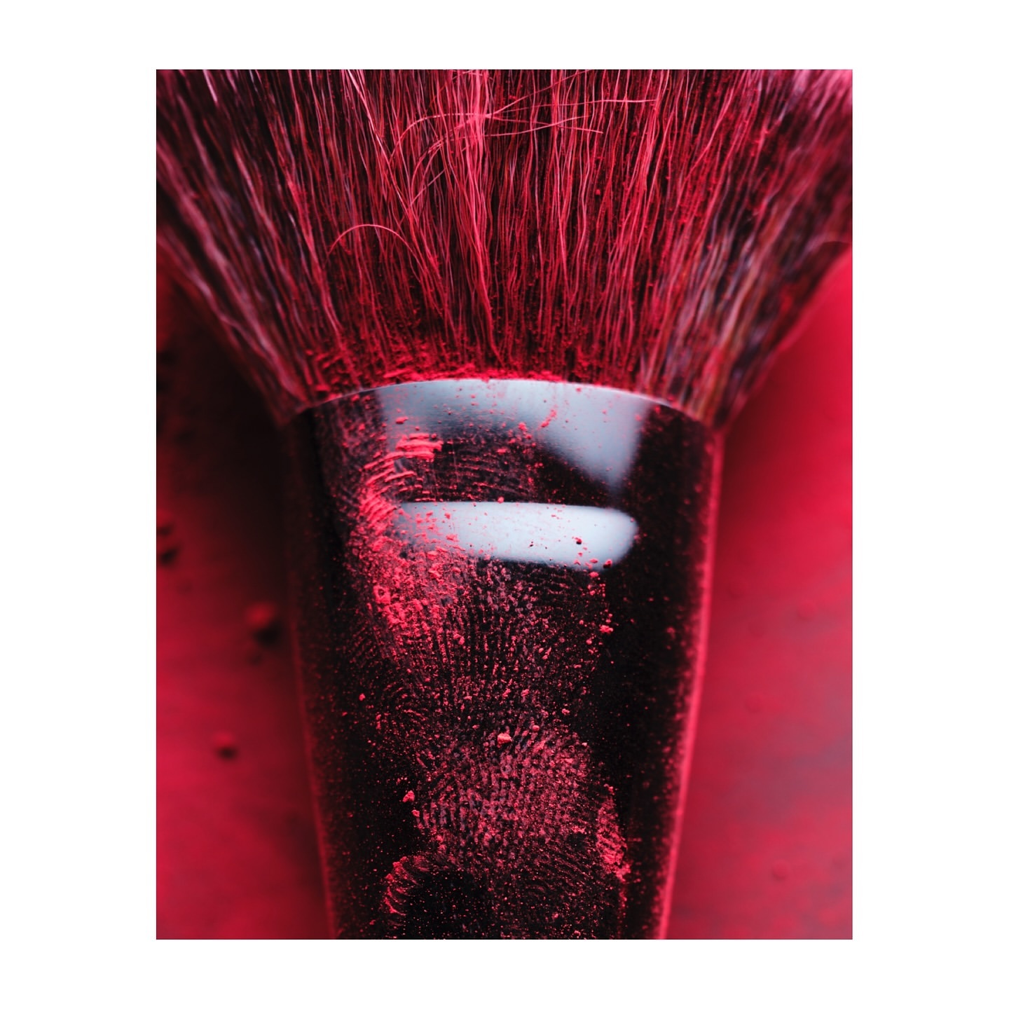 Close-up of a makeup brush with black handle and pink bristles on a pink surface covered in loose powder makeup.