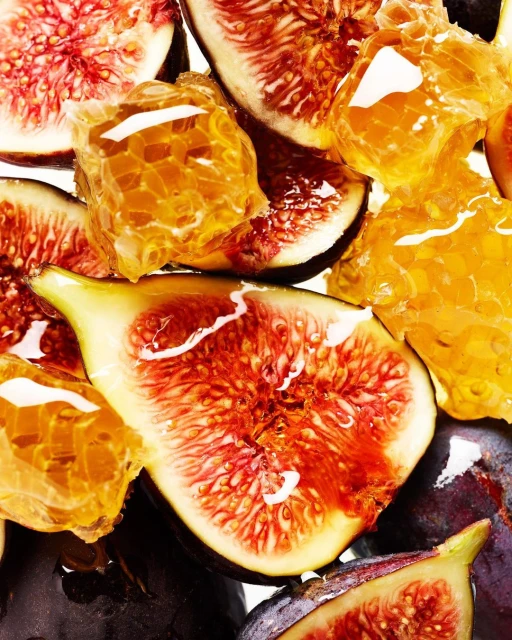 Close-up still life of sliced figs and honeycomb pieces glistening with liquid, showcasing vibrant colors and textures on a white surface.