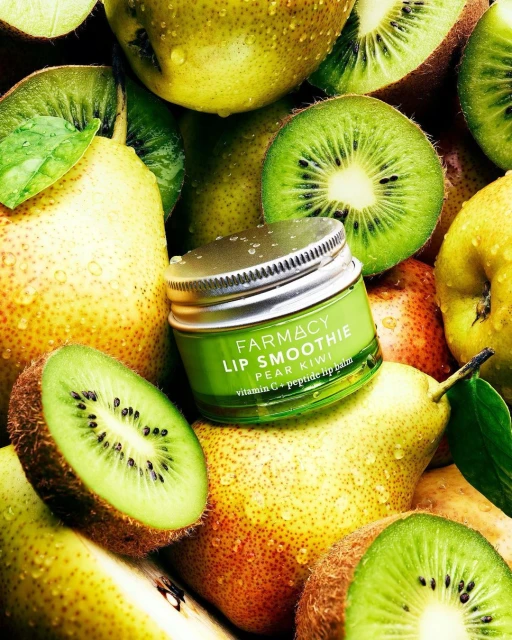 Close-up of Farmacy Lip Smoothie Pear Kiwi balm surrounded by fresh pears and kiwis, emphasizing natural beauty and skincare.