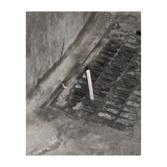 Angled shot of a metal grate set in concrete, with a small white tube protruding from one of the grate openings.
