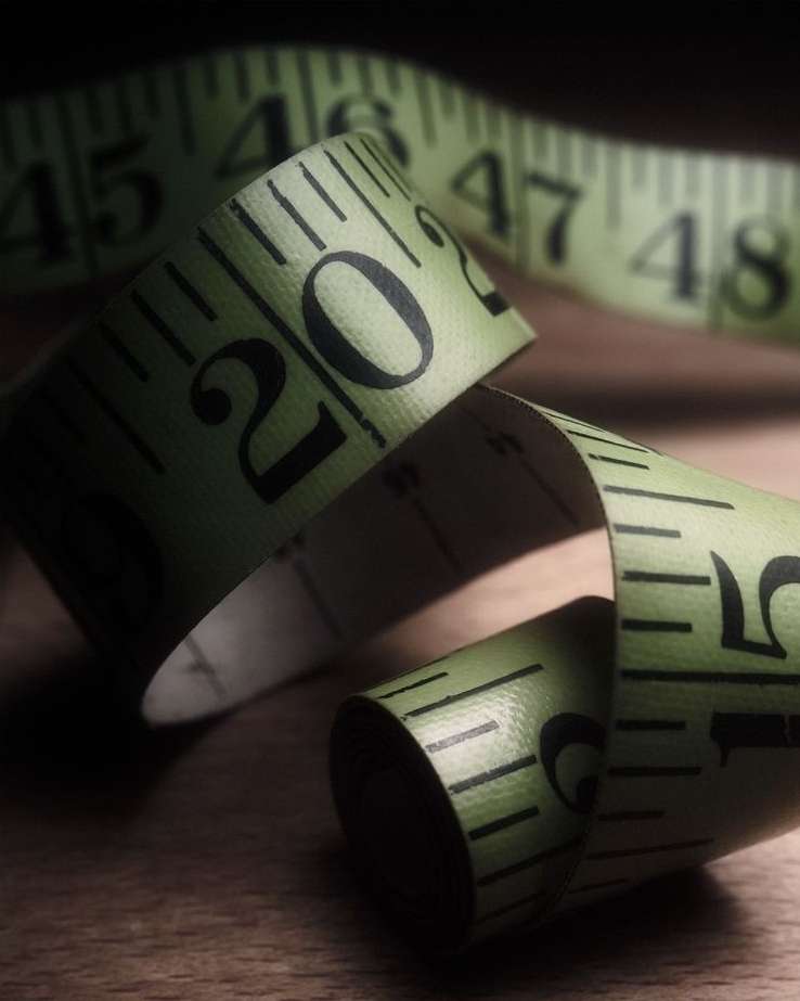 Close-up of a green and white measuring tape with black numbers, curling on a wooden surface in a studio setting.
