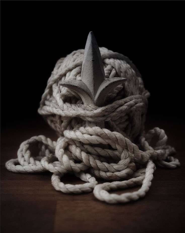 Rope ball with a finial on a wooden surface against a dark backdrop, creating a still life with contrasting textures and shapes.