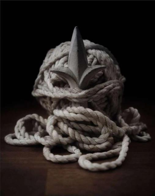 Rope ball with a finial on a wooden surface against a dark backdrop, creating a still life with contrasting textures and shapes.