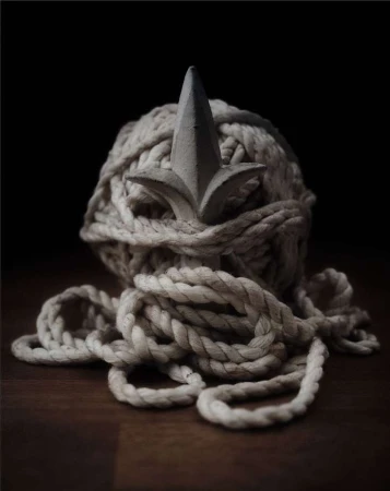 Rope ball with a finial on a wooden surface against a dark backdrop, creating a still life with contrasting textures and shapes.