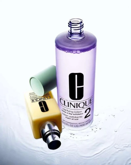 Two Clinique clarifying lotion bottles are angled with one laying down and another standing up on a glossy white surface.