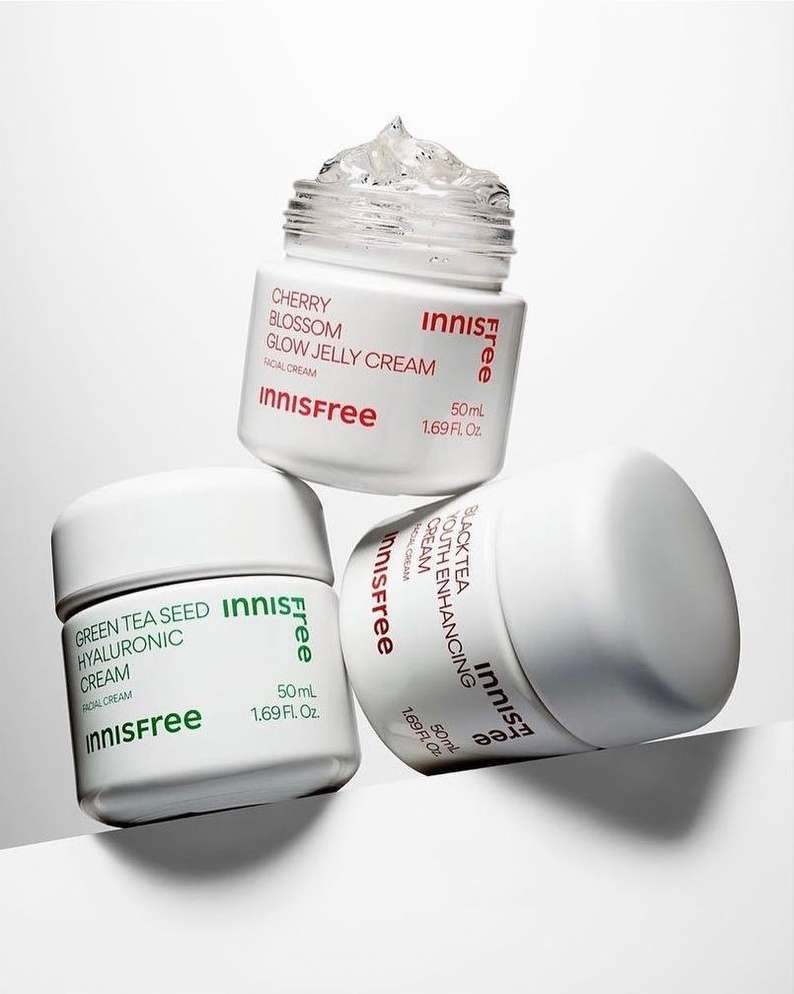 Three Innisfree skincare cream jars stacked in a pyramid, white background, featuring cherry blossom, green tea seed hyaluronic, and black tea youth enhancing creams.
