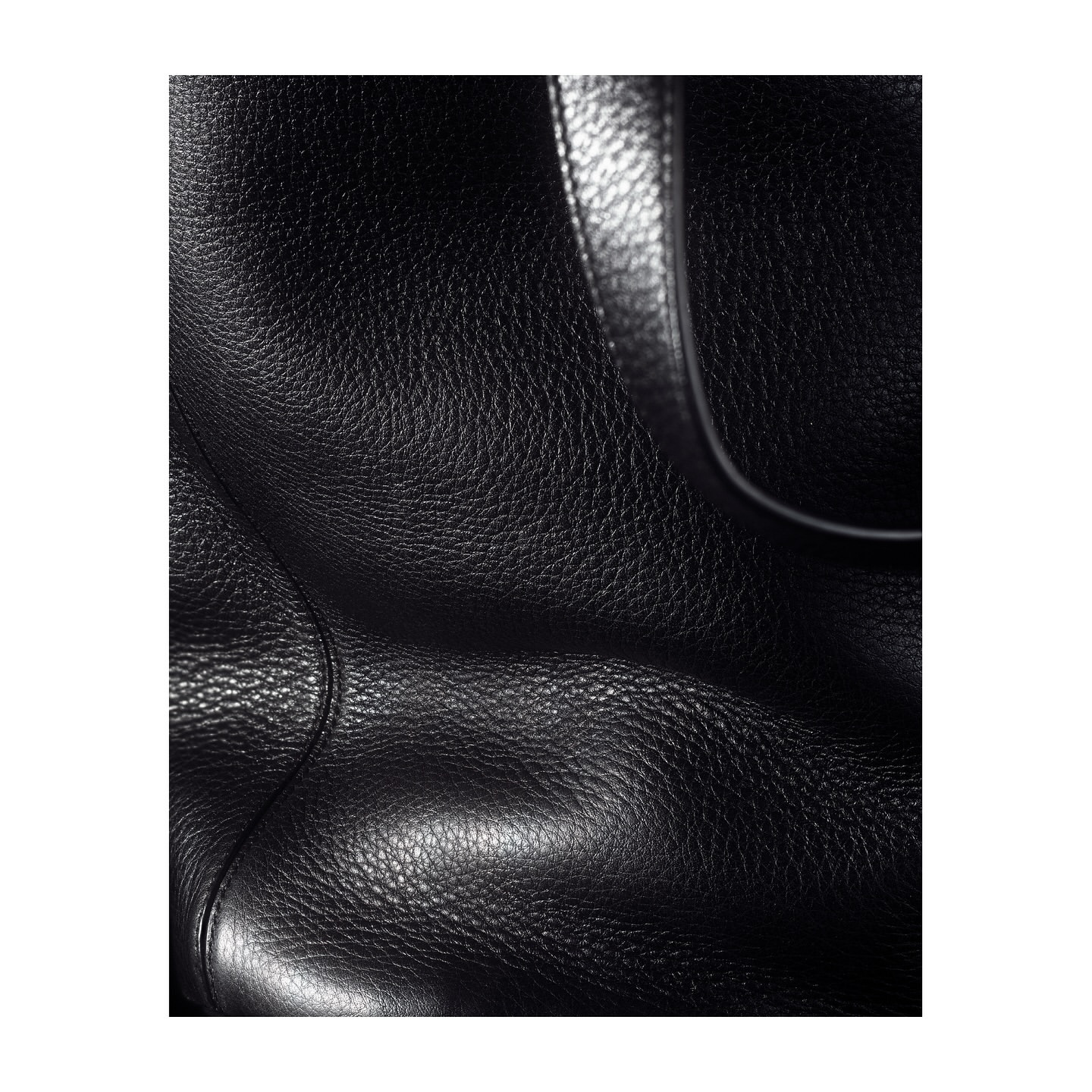 Close-up photograph of a black leather bag's surface showing its texture and a portion of its handle, set against a plain backdrop.