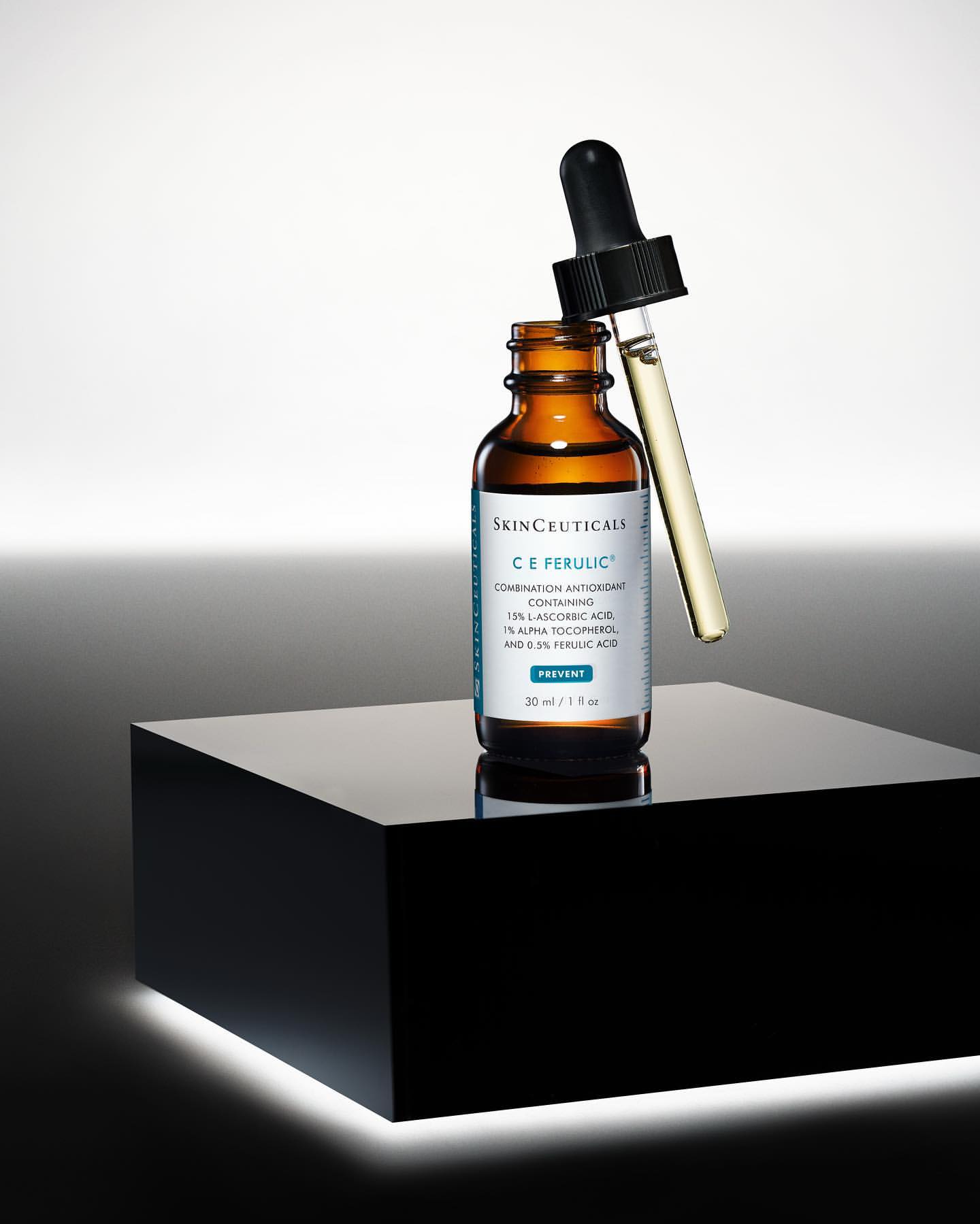 Skinceuticals C E Ferulic serum bottle with a dropper displayed on a glossy black cube against a gradient grey background.