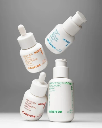 Four white Innisfree serum bottles are suspended mid-air against a plain grey backdrop, showcasing skincare and beauty product presentation.