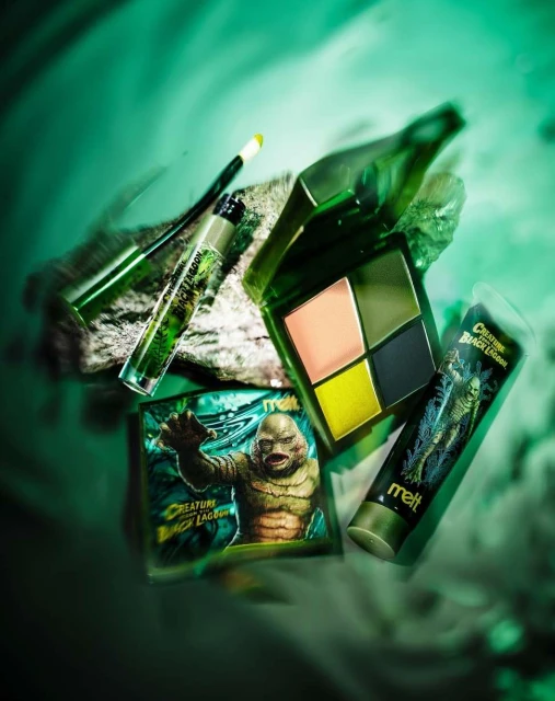 Cosmetic product range featuring 'Creature From the Black Lagoon' makeup palette and accessories, displayed on a stone surface, studio shot.