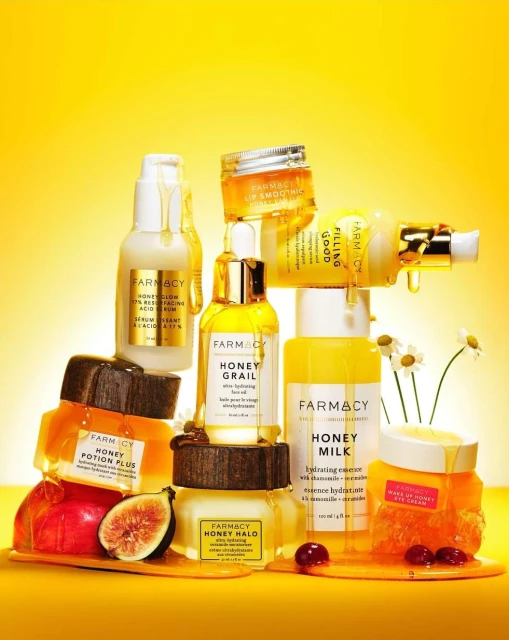 Elevated product shot of Farmacy skincare atop fruit, spilling honey, against a vibrant yellow backdrop, highlighting natural beauty ingredients.