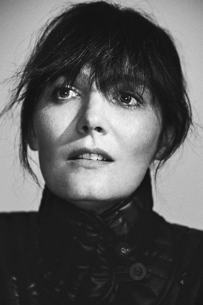 Monochrome portrait of a woman with bangs, wearing a dark jacket, captured with a close-up shot in a photo studio setting.
