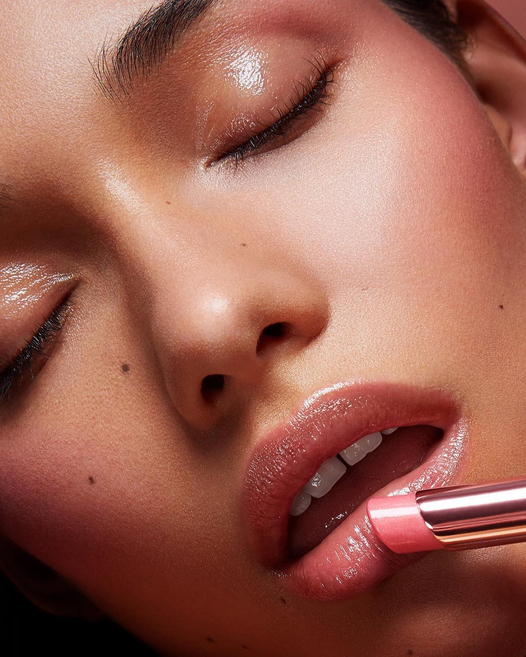 Close-up of a woman applying pink lipstick; beauty shot focusing on skincare, lips, and makeup, captured with soft, diffused lighting.