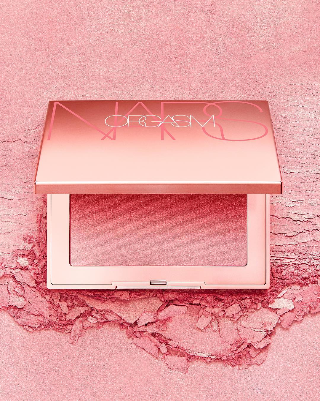 NARS Orgasm blush powder compact, a cosmetic product, is showcased with a pink powder background in a beauty product shot.