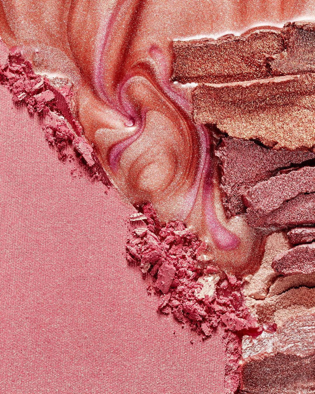 Close-up of crushed pink and bronze eye shadow with swirls of pearlescent liquid, creating a textured makeup product background.