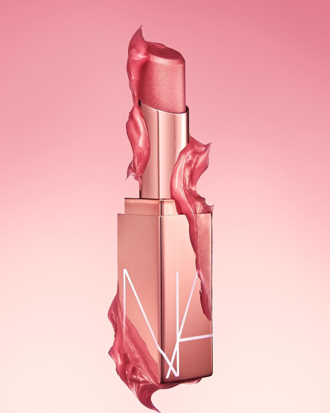 Close-up studio shot of NARS lipstick with pink shimmer, surrounded by matching glossy gel, against a soft pink background, beauty and glamour.