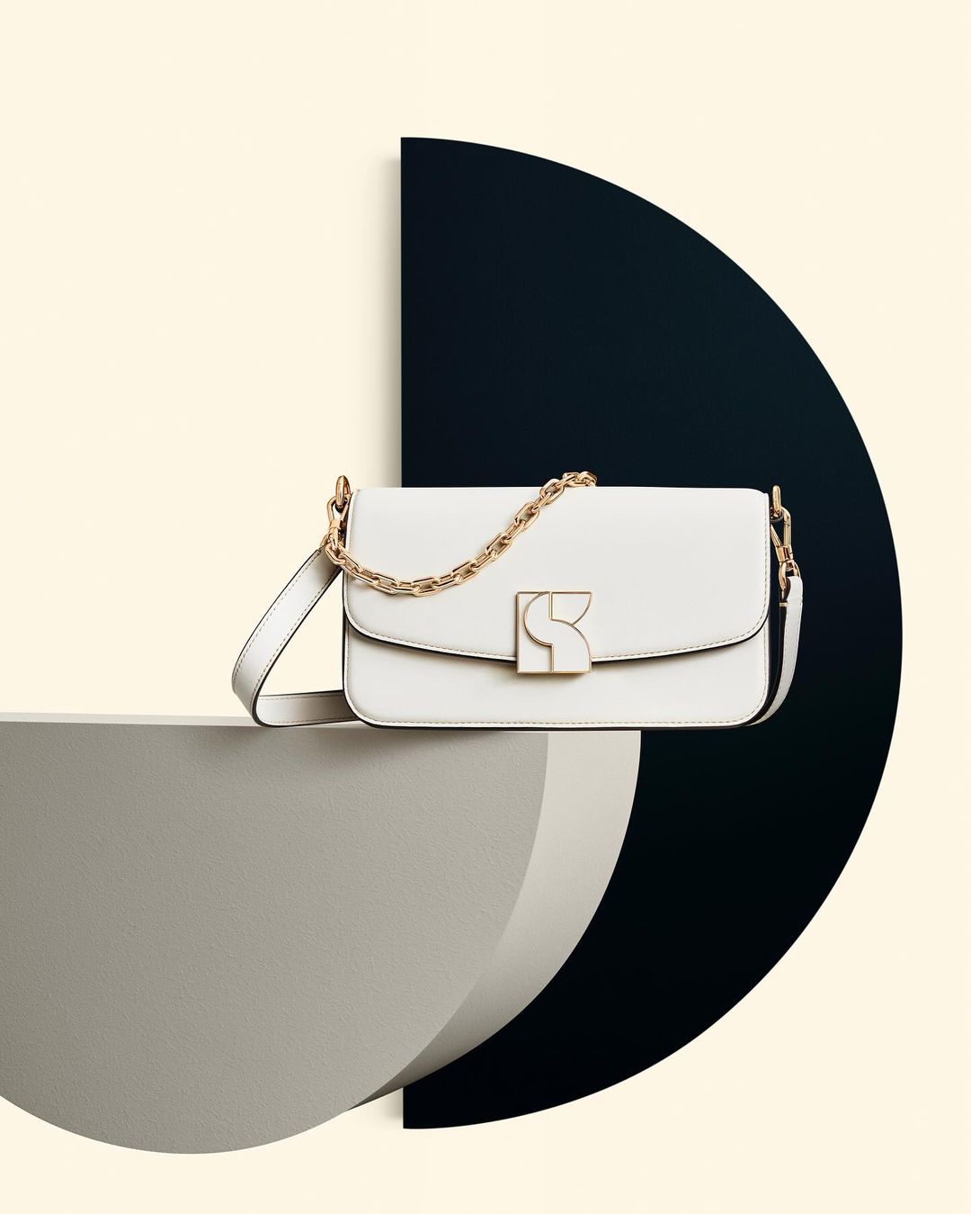 Elegant white leather shoulder bag with gold chain and hardware, displayed on geometric grey and black platform against a light cream backdrop.