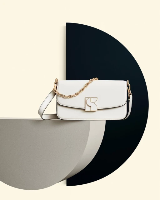 Elegant white leather shoulder bag with gold chain and hardware, displayed on geometric grey and black platform against a light cream backdrop.