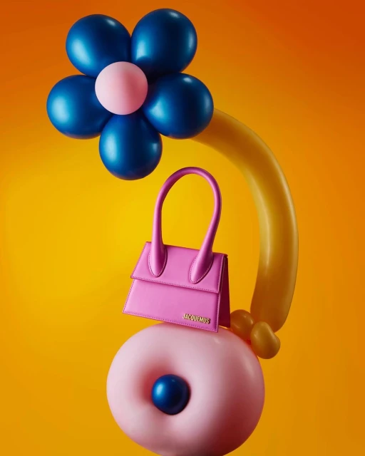 Pink Jacquemus purse atop a donut-shaped balloon with a blue-and-pink flower balloon arrangement, set against a vibrant yellow background.