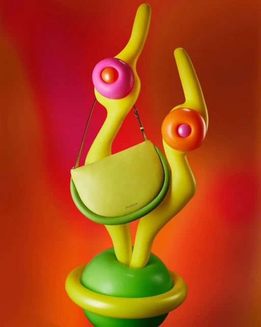 Stylish chartreuse purse with a curved shape on a decorative yellow stand with orange and pink accents against a pink and orange background.