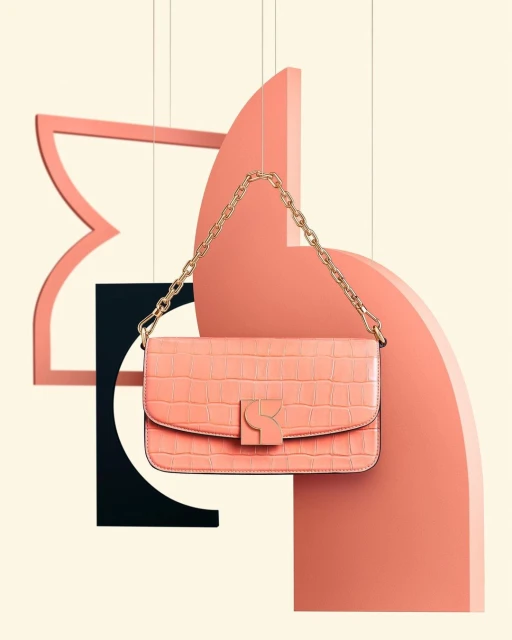 A coral-colored, mock-crocodile purse with a gold chain hangs in front of geometric shapes in shades of coral and black against a cream background.