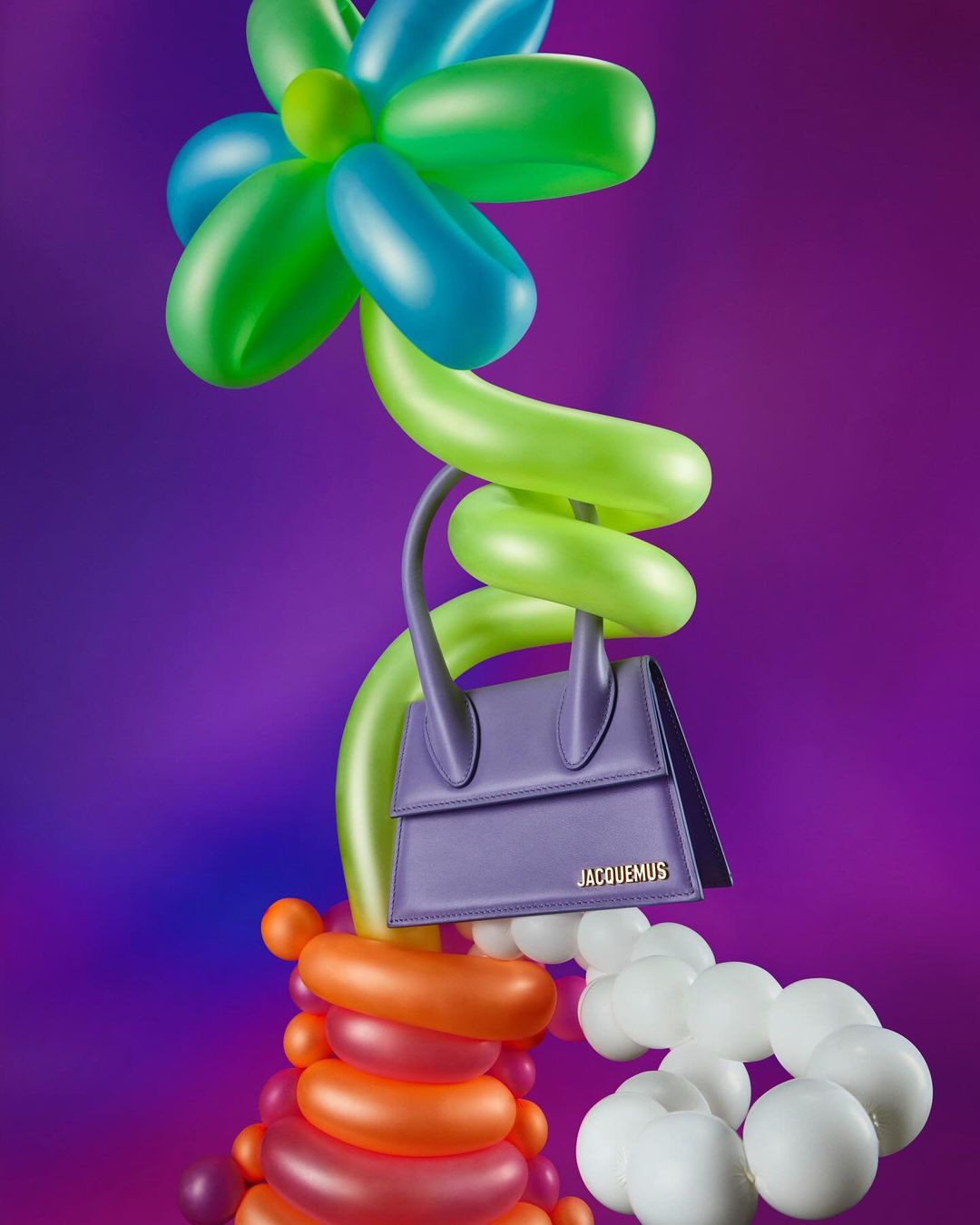 Fashion handbag displayed on a balloon flower sculpture against a gradient purple background in a studio product shot for accessories.