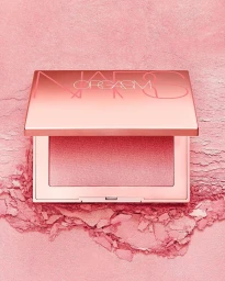 Close-up product shot of a metallic pink blush compact surrounded by loose shimmering pink powder pigment.