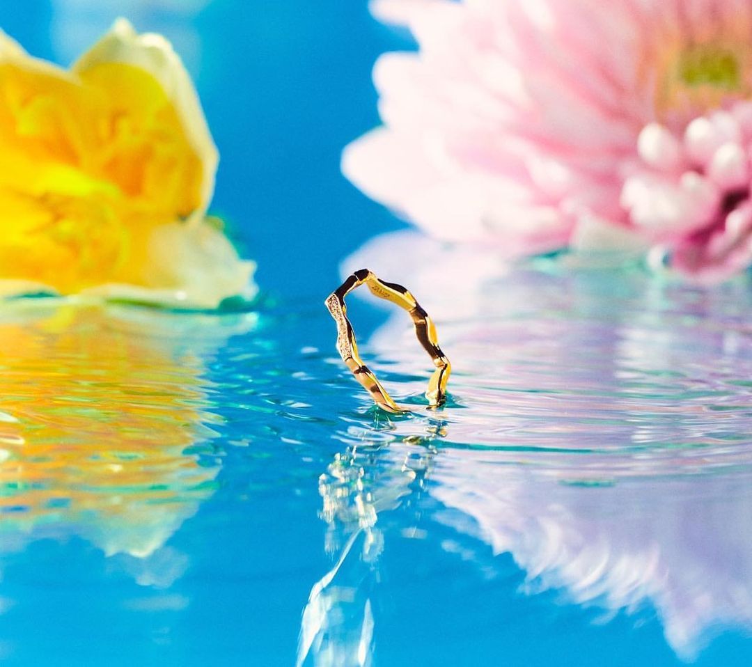 Gold ring resting in water with yellow and pink floral reflections under bright sunlight by Laia Benavides