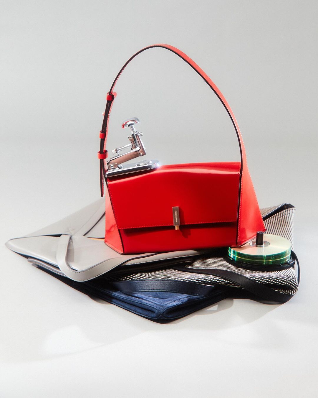 Studio shot of a red purse with a stapler on top of it, placed on top of two folded bags against a neutral background.