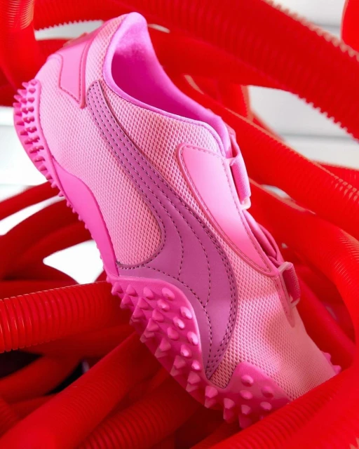 Close-up of a pink Puma track shoe with Velcro closure, contrasted against vibrant red ribbed tubes. Focus on athletic footwear.