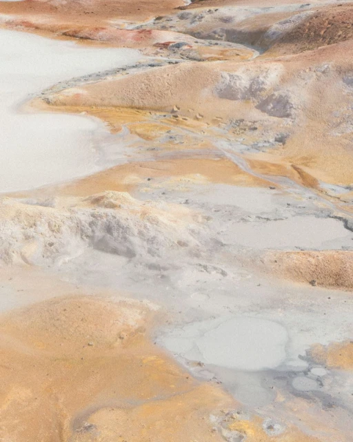 Geothermal landscape featuring tan and white earth, water pools, and mineral deposits in an outdoor setting, with geothermal activity.
