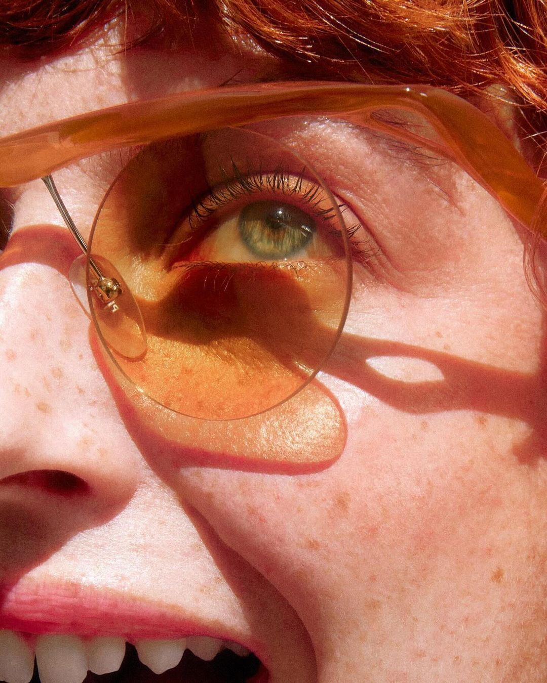 Close-up portrait of a young fair-skinned adult female with reddish-brown hair wearing round glasses, her green eye prominent.