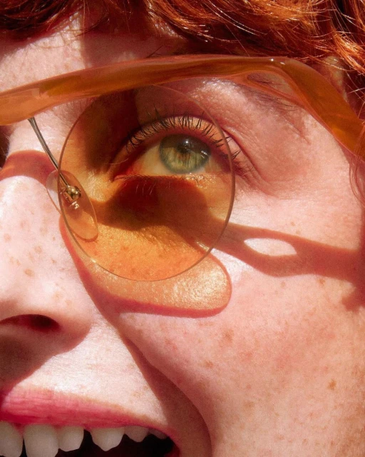 Close-up portrait of a young fair-skinned adult female with reddish-brown hair wearing round glasses, her green eye prominent.