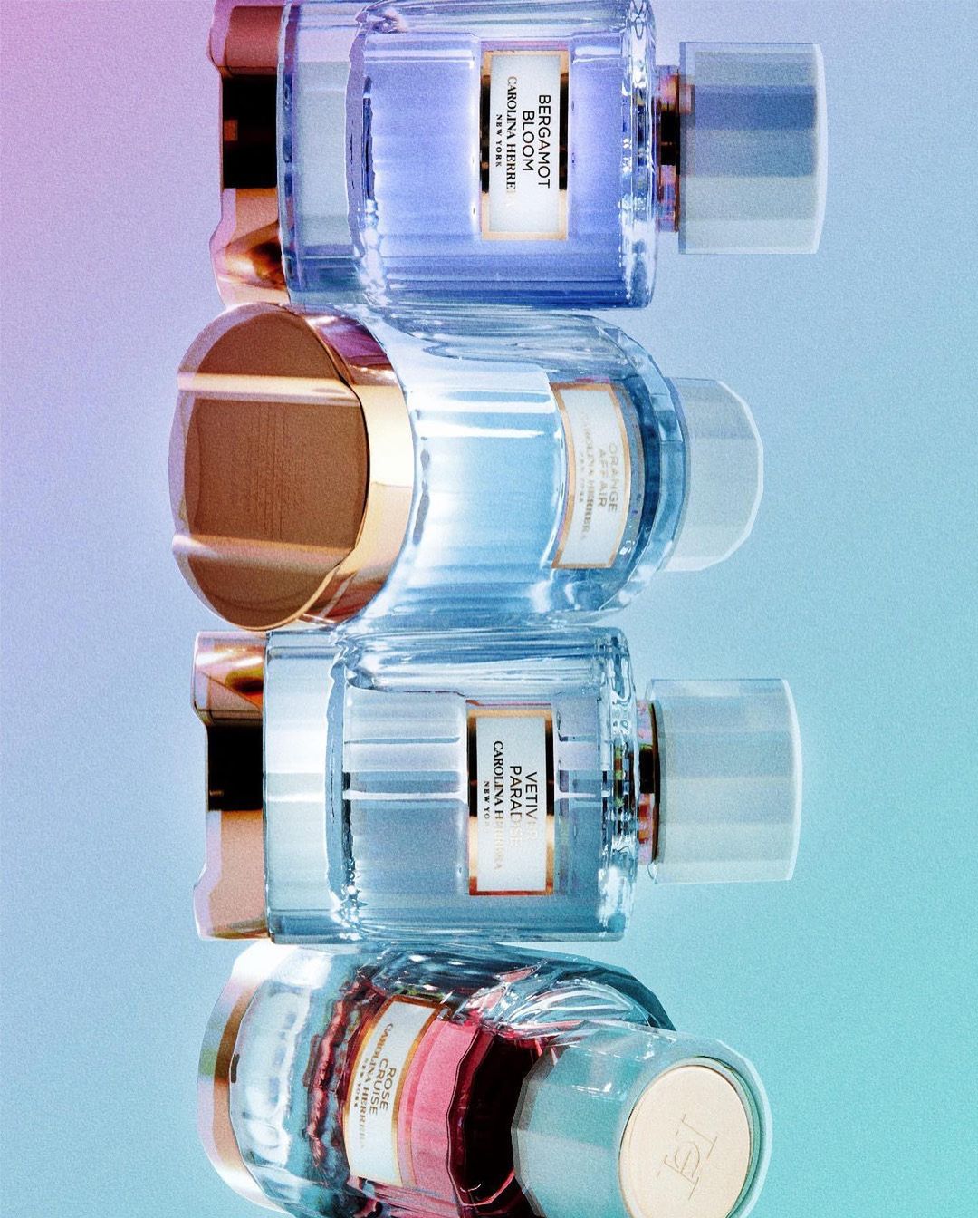 Close-up of stacked Carolina Herrera fragrance bottles in varying colors, set against an ombre background ranging from pink to blue.