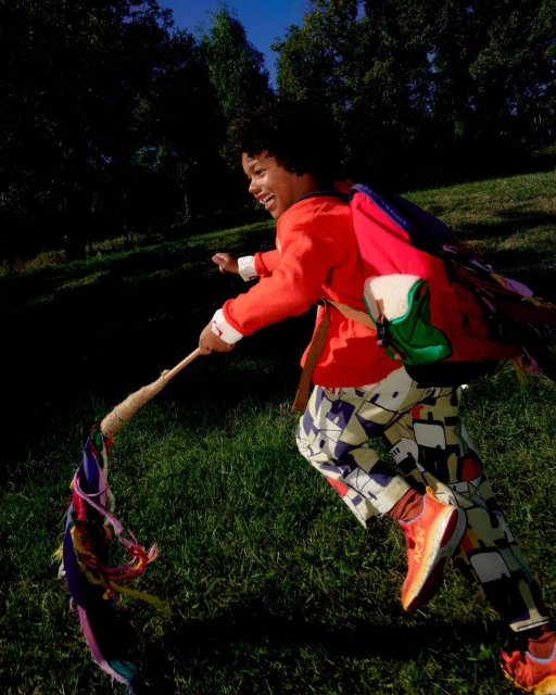 A child joyfully runs through a grassy field, holding a colorful streamer, with a forest backdrop under a vibrant blue sky.