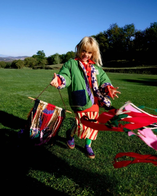 A young child joyfully plays outside on a sunny day, holding a colorful banner-like object with streamers in a grassy field.