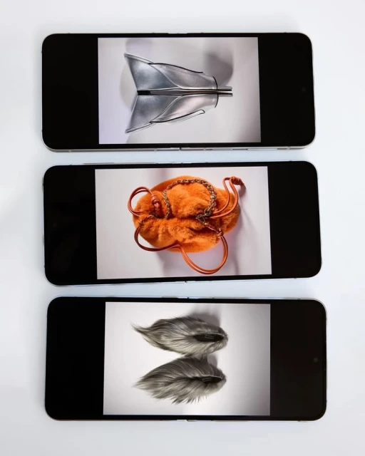 Three smartphones display fashion accessories against white backgrounds. A silver purse, an orange handbag, and gray earmuffs are shown.